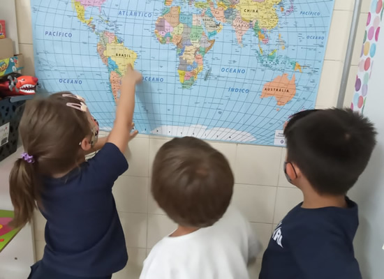  Imagem de crianças da Educação Infantil aponatando para o mapa do mundo fixo na parede 